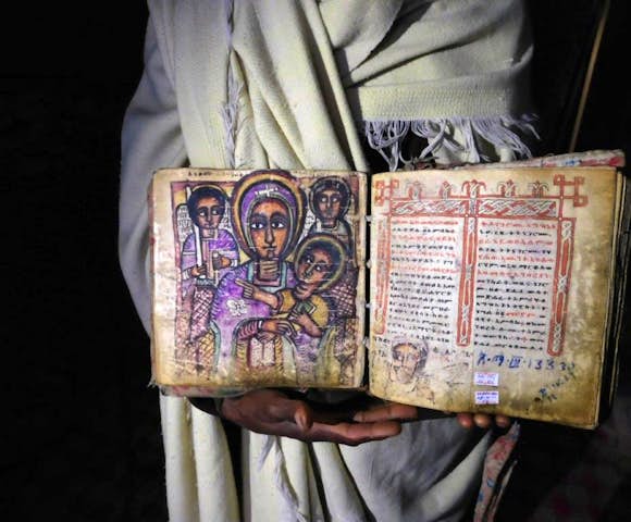 Priest holding ancient manuscript inside rock-hewn churches of Lalibela in Ethiopia