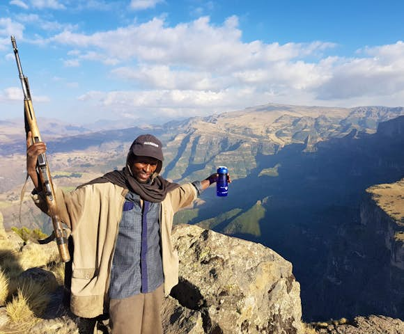 Scout with rifle spreading arms in front of landscape in the Simien Mountains